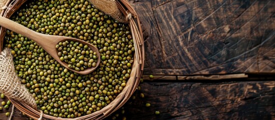 Poster - Top view of a basket containing raw mung beans and a wooden spoon on a wooden background, with copy space image.