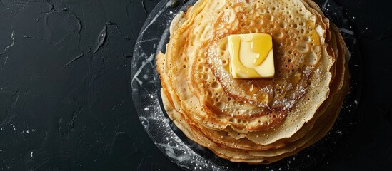 Poster - Top view of a stack of crepes with butter on a marble board against a black background, featuring copy space image.