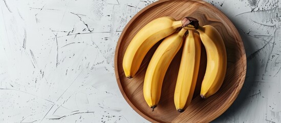 Poster - Yellow bananas with copy space image on a wooden plate against a white background showcasing a nutritious tropical fruit from above