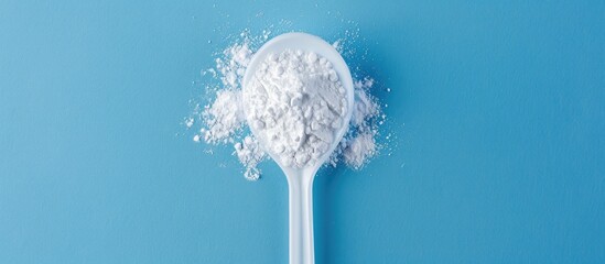 Poster - White powder in a plastic spoon arranged on a blue background in a composition ideal for adding text suitable for display with copy space image
