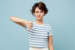 © ViDi Studio - Young sad displeased mad woman she wears striped t-shirt casual clothes showing thumb down dislike gesture isolated on plain pastel light blue cyan color background studio portrait. Lifestyle concept.