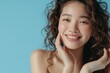 © SHI - Beautiful Asian beauty with long curly hair, Korean makeup, radiant complexion, healthy facial skin, portrait smile, looking at the mirror on an isolated blue background.