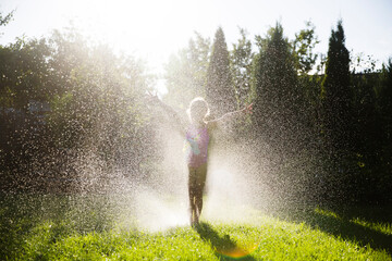 happy child girl playing with garden hose and having fun with spray of water in sunny backyard. summ