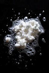 Sticker - A close-up shot of a pile of white foam sitting atop a dark, black surface