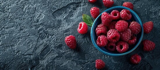Poster - Top down view of ripe raspberries in a blue bowl on a rugged black backdrop with space for text or images in the scene. copy space available