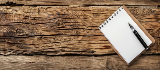 Fototapete - Office wooden table with a pen placed on a blank notepad offering a copy space image