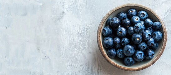 Poster - Top view of a bowl filled with blueberries on a wooden surface against a white concrete background with copy space image