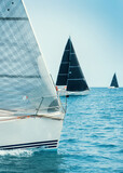 Sailboats races in regatta near Brindisi under blue cloudless sky. Boats have white and black sails