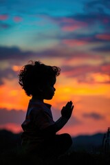 Canvas Print - A young child sitting on a hill with a beautiful sunset in the background