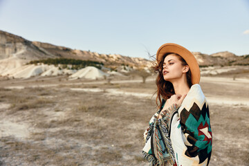 Wall Mural - Desert wanderlust woman in hat and blanket standing amidst mountains in the arid landscape