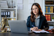 © apichat - A woman in a suit is sitting at a desk with a laptop and a pen