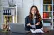 © apichat - A woman in a suit is sitting at a desk with a laptop and a stack of papers