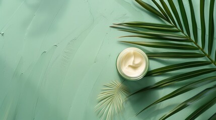 Canvas Print - Cosmetic cream jar with palm leaf on green background flat lay