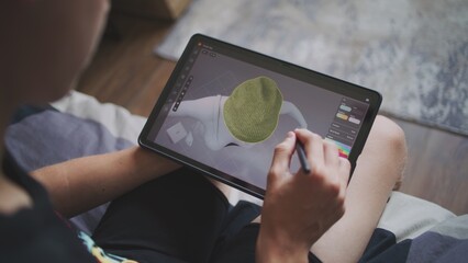 Fototapete - Boy with digital stylus and tablet in hands sits at home, creates 3d models. Focused teenager draws clothes for game character using 3d modeling program. Development and game design concept. Close up.