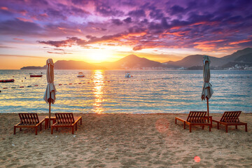 Wall Mural - Captivating sunset at beach with chaise lounges and umbrellas in Sveti Stefan near Budva.