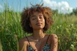 © ArtMajestic - Young black african american curly head woman enjoying sunny day, relaxing under suns rays. Outdoor setting in field with green grass. Concept of summer atmosphere, peaceful moment