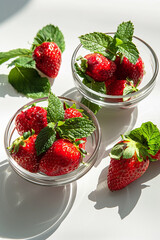 Canvas Print - Fresh strawberries with mint leaves in glass bowls, bathed in natural sunlight, showcasing a healthy summer snack.