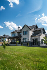 Elegant suburban house with a spacious front yard and bright blue sky. The house has a stone and siding exterior with manicured landscaping, emphasizing luxury living.