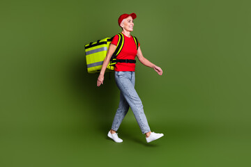 Canvas Print - Full body photo of mature woman delivery employee thermo bag walking wear red uniform workwear isolated on khaki color background