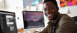 © Ai Studio - A young man with a warm smile sits in front of a computer, appearing engaged in his creative work in a bright, modern office setup.