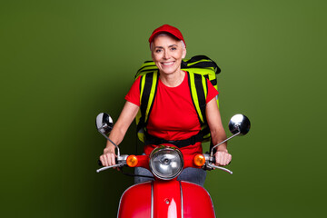 Poster - Photo of senior female professional delivery employee thermo bag ride scooter wear red uniform workwear isolated on khaki color background