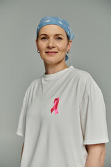 A woman with short hair wears a white shirt with a pink ribbon, symbolizing breast cancer awareness.