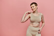 © LIGHTFIELD STUDIOS - A woman with short hair, wearing a beige bra, stands against a pink background.