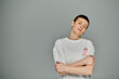© LIGHTFIELD STUDIOS - Short-haired woman in white t-shirt with pink ribbon, arms crossed on grey background