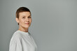 © LIGHTFIELD STUDIOS - A woman with short hair standing against a grey background, confidently looks towards the camera.