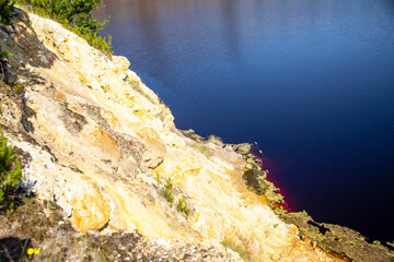 Contrast between the rocky wall with mineral residues and the blue water, Solfatara area, Pomezia, Rome, Italy