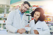 © TamJam/peopleimages.com - Man, woman and checking box in pharmacy for prescription drugs, ingredients or medical benefits of pills. Healthcare, pharmacist and consultant reading info on medicine for advice, decision or choice