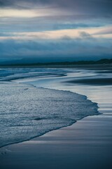 Wall Mural - Serene beach scene with gentle waves lapping the shore under a cloudy sky at dusk