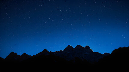 Wall Mural - A mountain range is silhouetted against a dark sky with a few stars visible