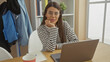 © Krakenimages.com - A young hispanic woman with glasses working on a laptop at home, looking calm and casual in a striped shirt.