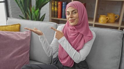 Wall Mural - Beautiful hispanic woman wearing a hijab gesturing in a modern living room interior.