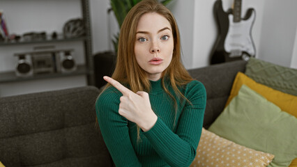 Poster - Young caucasian woman in a green sweater points something out in her modern living room