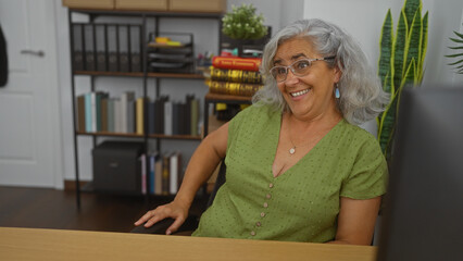 Poster - Woman smiling in a workplace, indoor setting with grey hair and glasses, surrounded by books and plants in an office environment