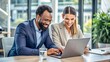 © Matan - Two smiling diverse businesspeople using a laptop together at wo