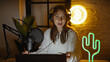 © Krakenimages.com - Young caucasian woman podcasting in a studio with a neon bitcoin sign and cactus decoration.