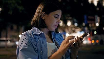 Wall Mural - Young beautiful hispanic woman smiling happy using smartphone in the streets at night