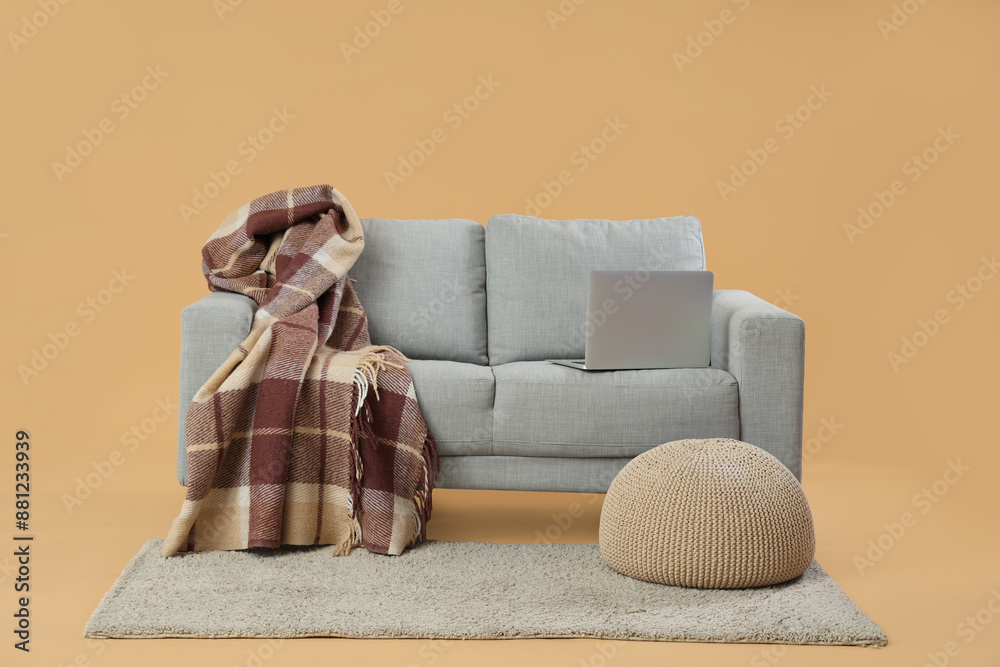 Modern living room interior with grey sofa, laptop and wicker pouf on beige background