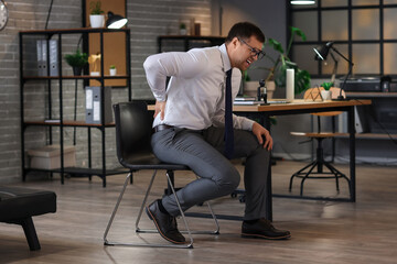 Wall Mural - Young businessman suffering from back pain in office at night