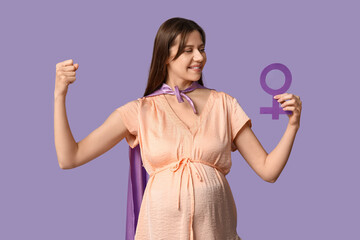 Canvas Print - Beautiful young pregnant woman in superhero cape with gender symbol showing muscles on lilac background