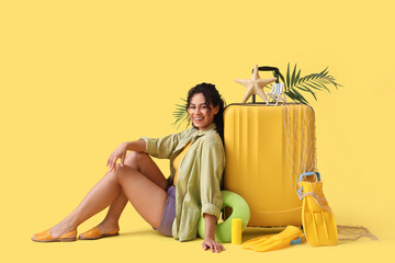 Wall Mural - Young African-American woman near suitcase with accessories on yellow background