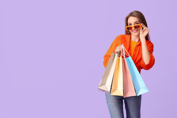 Poster - Young woman in sunglasses with shopping bags on lilac background