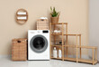 © Pixel-Shot - Modern washing machine with rack and baskets near beige wall
