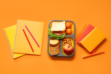 Wall Mural - School supplies, lunch box with sandwich and apple on orange background. Top view