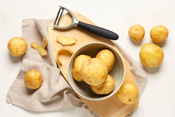 Wall Mural - Bowl with raw potatoes and peeler on white background