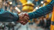 © tashechka - Two people shaking hands in an industrial manufacturing setting, highlighting partnership, agreement, and teamwork in a professional environment.