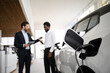 © sofiko14 - Car salesman discusses electric SUV with businessman. Charging station and modern vehicle highlight eco-friendly options. Professional interaction emphasizes business deal in automotive industry.